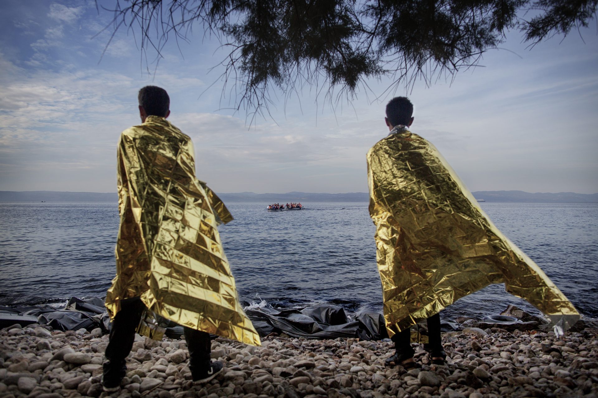 Two men who have just arrived on the Greek island of Lesbos use foil blankets to get warm and dry as they watch two inflatable boats with Syrian refugees approaching the beach coming from the Turkish coast. © Espen Rasmussen / VII.